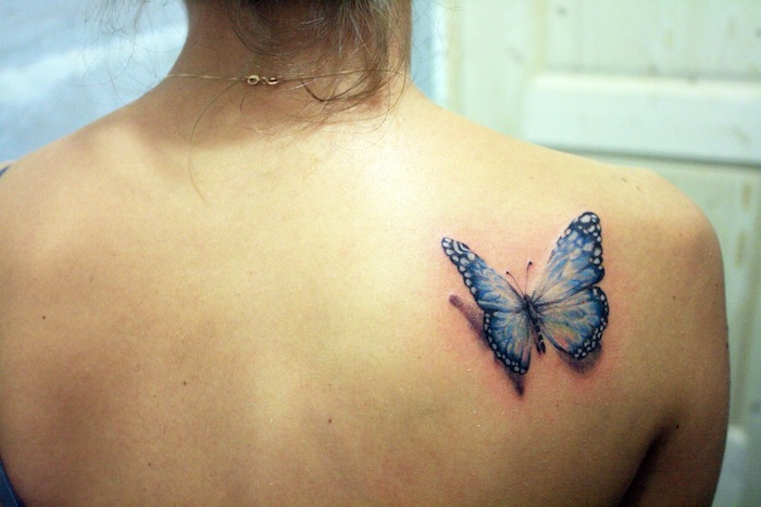 tatouage papillon 3d, collier en or, cheveux brun attachés, dessin papillon bleu
