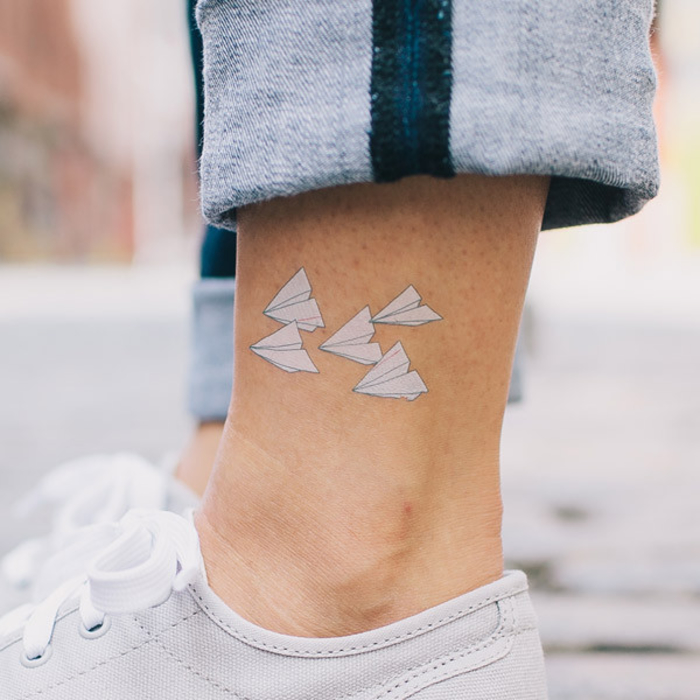 un tatouage minimaliste temporaire à l'encre blanche composé de petits avions en origami