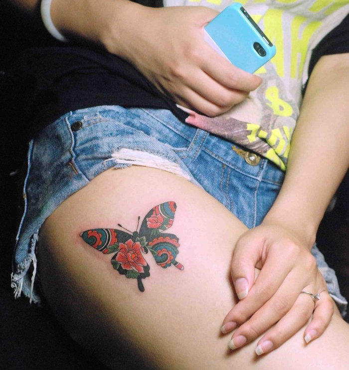 tatouage symbolique, paire de jeans en denim avec t-shirt noir, bague femme avec cristal, tatouage papillon en rouge et noir