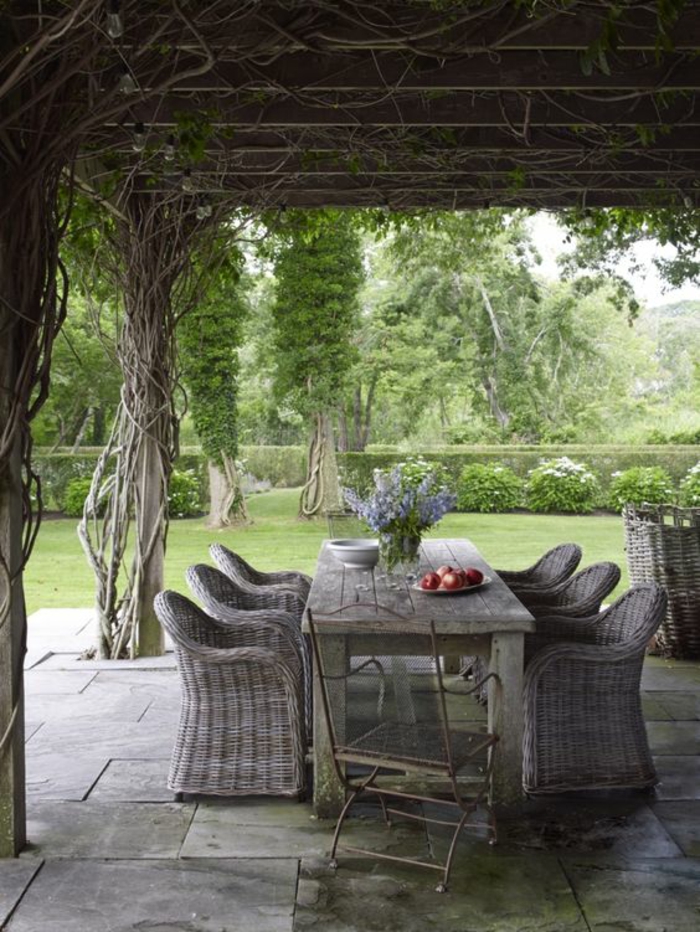 terasse couverte avec des fauteuils en rotin et une table en bois grise ambiance romantique