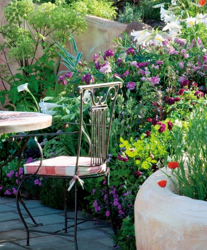 une végétation florissante, disposée à l anglaise, plusieurs arbustes fleuris, fleurs, salon de jardin, constitué de table et chaise en metal