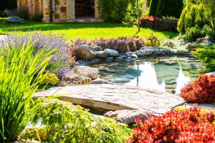 amenagement jardin exterieur avec un étang et un pont en pierre, plusieurs pierres, arbustes et arbres