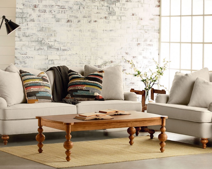 tapis couleur ecru, revêtement sol, canapé et fauteuil gris, table basse bois vintage, mur de briques blanchis, coussins bohème