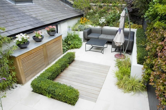 idee salon de jardin, canapé et table gris sur une terrasse zen, revêtement bois, carrelage, parasol, buis, arbustes et arbres, gravier en bordures