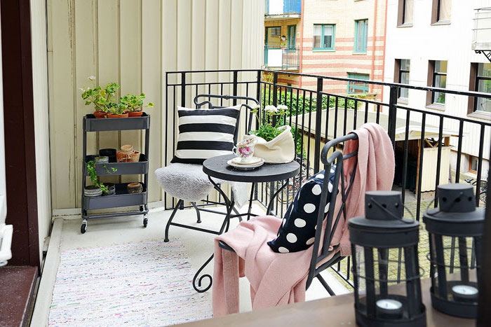 aménager une terrasse avec balustrade noire, tapis cocon, chaises et table metallique noire, étagère fleurs, lanternes noires