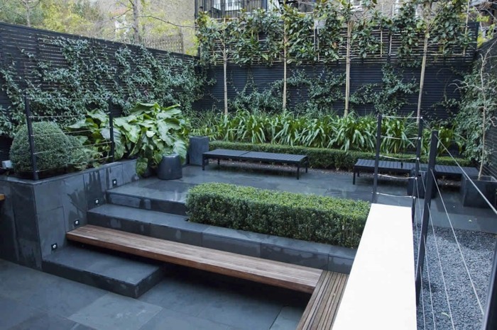 aménager sa terrasse, revêtement gris, zone de gravier gris, banc noirs, buis et arbustes, plantes grimpantes sur une clôture
