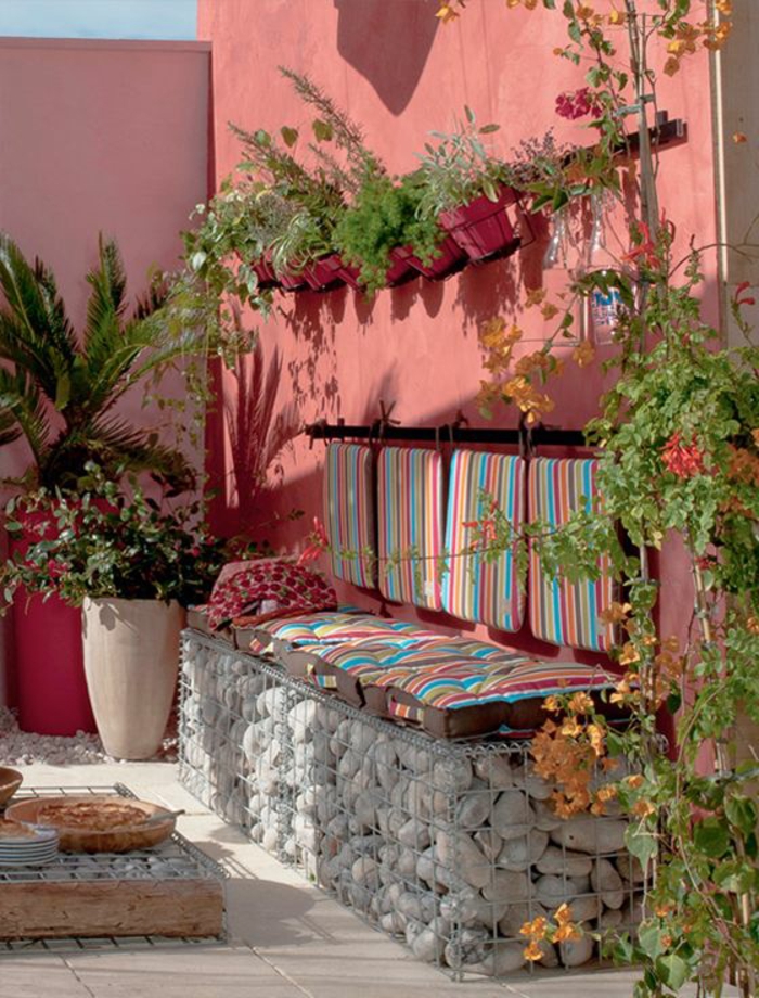 exemple d aménagement de jardin avec des murs en couleur rose et des coussins pour le banc en pierre aux rayures pastels 