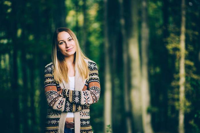 balayage-ombre-blonde-débardeur-blanc-paire-de-jeans-ceinture-marron-femme-dans-la-foret couleur de cheveux tendance, gilet beige à motifs flocons de neige marron et blanc, cheveux lisses ombré