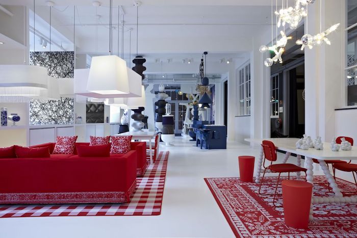 canapé rouge design dans un salon ouverte sur une cuisine, salle à manger, murs et sol blancs, coin repas bleu, suspensions originales