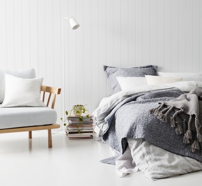 modele de chambre adulte cocooning revêtement sol et murs blanc, fauteuil en bois avec coussin d assise blanc, linge de lit blanc et gris, pile de livres