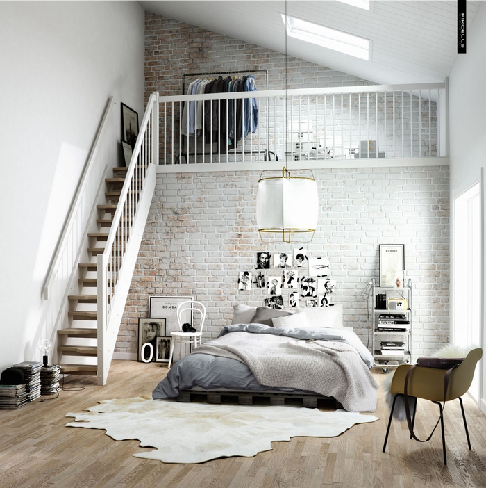 une chambre à coucher d'esprit loft tout en blanc équipée d'un lit en palette posé contré un mut en briques 