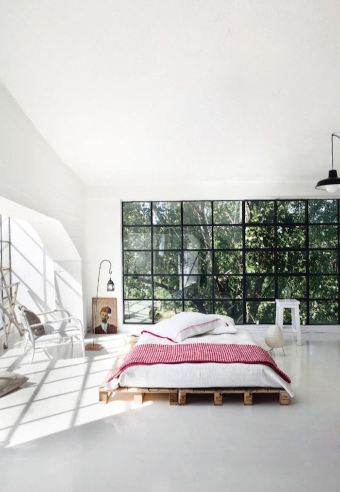 une chambre à coucher industrielle d'esprit loft avec un grand lit palette bois naturel et assez d'espace pour une circulation fluide