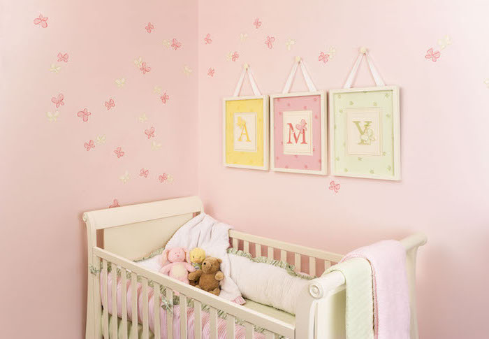 pièce aux murs rose avec décoration en papillon miniatures, serviette rose pastel sur lit bébé blanc