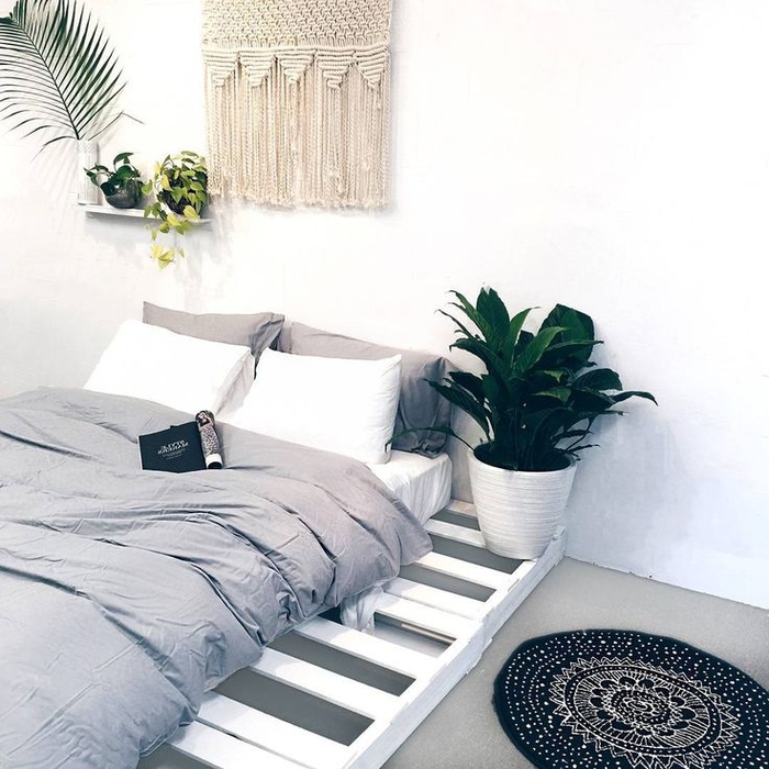 une chambre à coucher blanc et gris d'ambiance bohème chic avec un simple lit palette à sommier dépassant le matelas