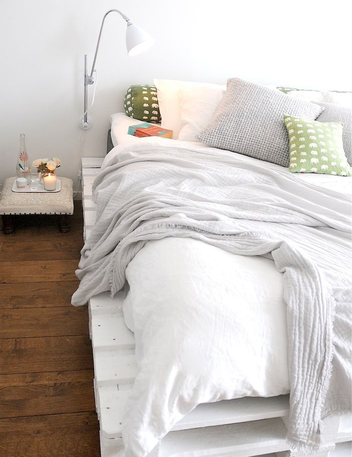 une chambre à coucher ensoleillée à déco minimaliste, avec un lit palette bois peint en blanc qui contraste avec le parquet