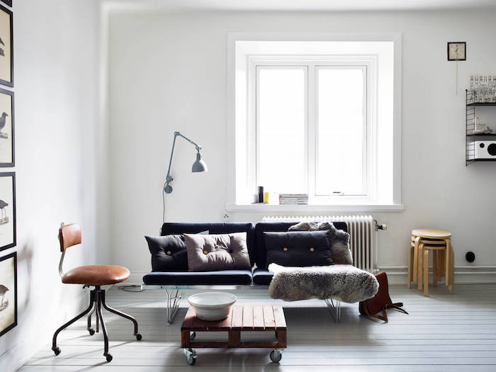 revêtement sol et murs blancs, canapé gris anthracite, table basse en palette à roulettes, jeté de fourrure, chaise en cuir marron