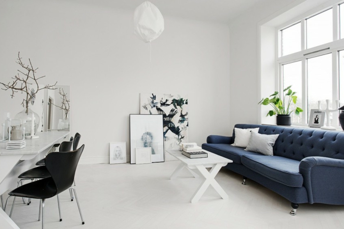 idée déco scandinave, décor tout en blanc avec un canapé bleu foncé contrastant, revêtement sol et murs blanc, table basse blanche, deco dessins graphiques, accessoires scandinaves