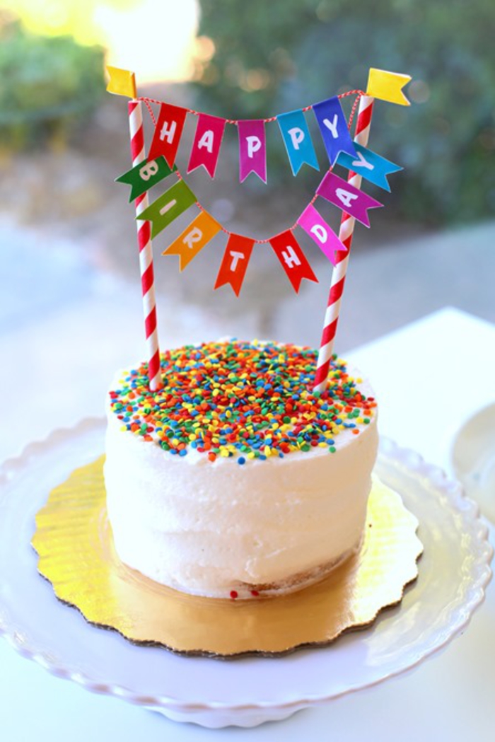 une décoration anniversaire colorée, gâteau d'anniversaire génoise moelleux recouvert de glaçage au crème et décoré de vermicelles et de petite guirlande de fanions