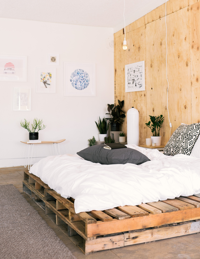 une chambre à coucher en blanc et bois de style bohème chic avec un lit palette et un mur en contreplaqué 