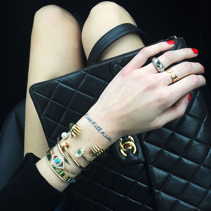 sac à main en cuir noir, manteau noir pour femme, bracelets en or avec perles et cristaux, petit tattoo sur la main