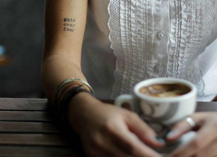 tatouage phrase, manucure noire sur ongles courts, chemise blanche sans manches avec boutons et décoration en dentelle