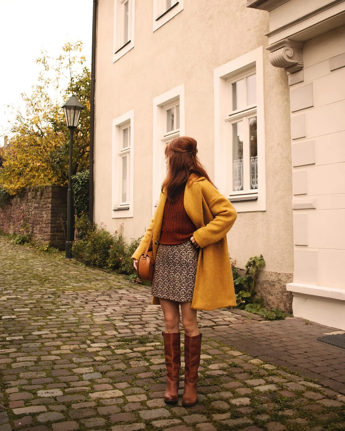 femme en manteau moutarde jupe courte pull marron bottes