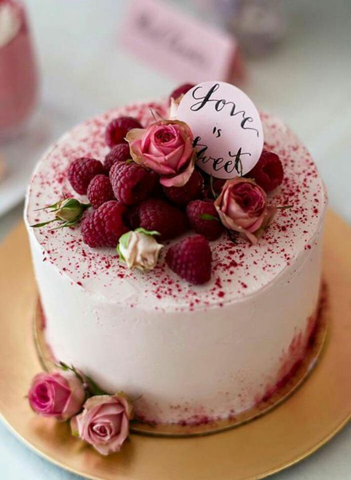gâteau d'anniversaire au glacage en couleur rose avec des framboises sur le dessus et décoré de vraies roses