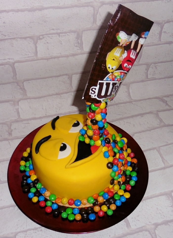 gâteau d'anniversaire avec la forme d'un grand bonbon jaune M and M's qui avale des bonbons au chocolat