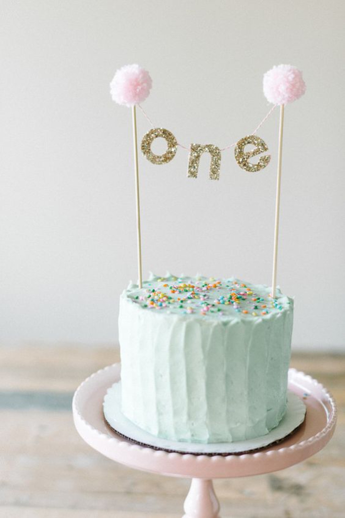 idée pour une décoration anniversaire originale en pom pom et guirlandes glitter, gateau anniversaire 1 an fille au glaçage pastel 