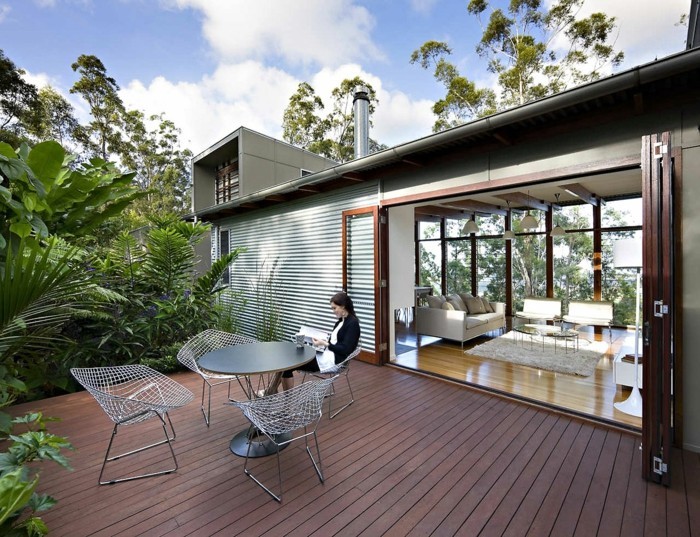 salon moderne qui s ouvre sur une terrasse zen en bois composite marron, table et chaises design, bordure de plantes vertes