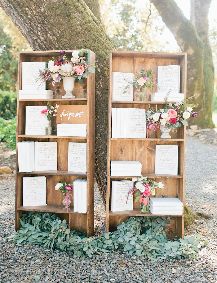 plan de table mariage en vieilles bibliothèques bois avec des livres blancs avec noms invités écrits sur la couverture, bouquets de fleurs dans des vases blancs