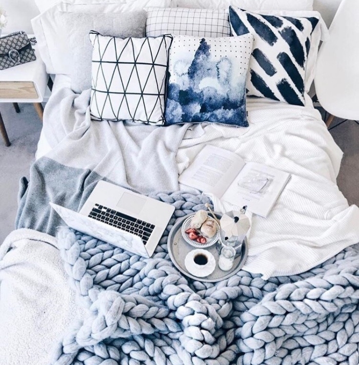 chambre cocooning avec linge de lit gris, bleu, blanc, coussins décoratifs, plaid tricoté à grosses mailles, petit déjeuner servi sur un plateau