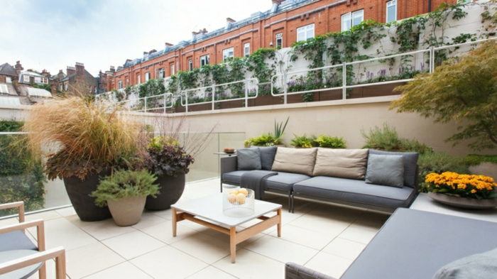 amenagement terrasse exterieure, carrelage beige, canapé gris, bacs à fleurs avec des plantes, table basse blanche
