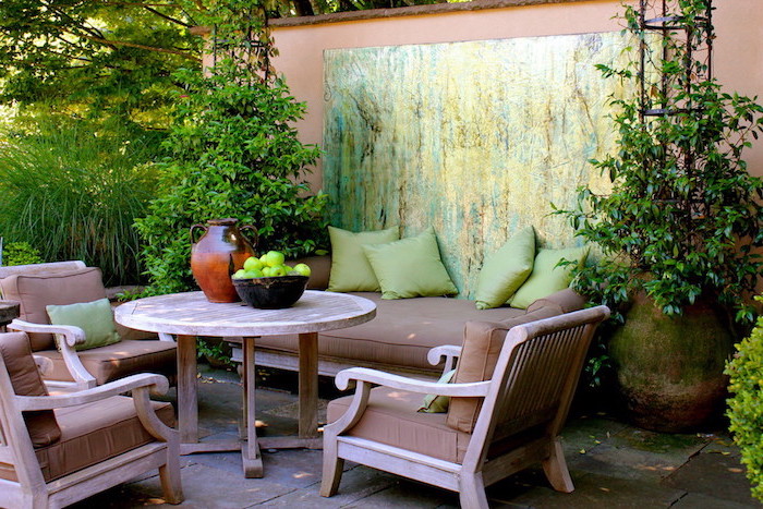 idee salon de jardin, table, fauteuils et canapé en bois avec des coussins d assise marron, coussins décoratifs verts, paysage de plusieurs plantes vertes