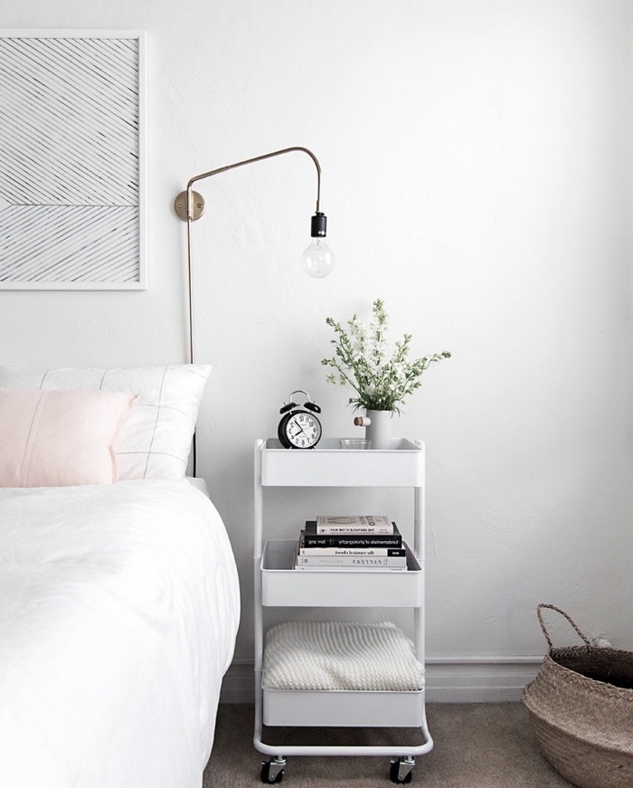 idee amengement chambre scandinave en blanc, avec coussin rose et table de nuit blanche à roulettes avec des étagères, tapis gris