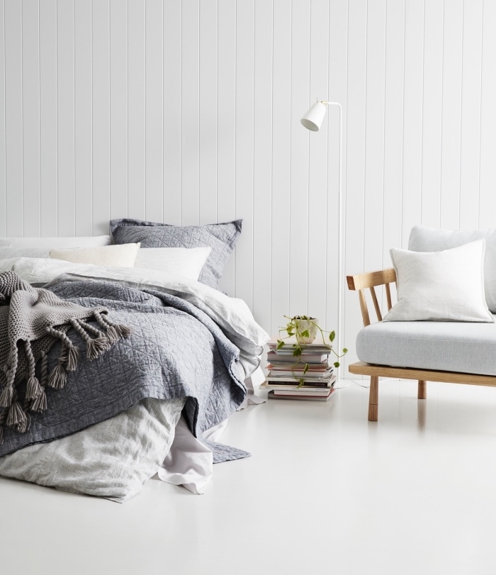 deco inspiration scandinave, mur lambris blanc, linge de lit blanc et gris, sol gris, canapé en bois clair avec coussin blanc, pile de livres