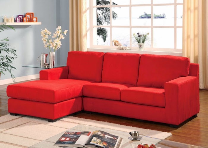canapé rouge vermillon dans un salon neutre, tapis et rideaux couleur beige, mur couleur bleu clair, parquet marron, table basse en verre