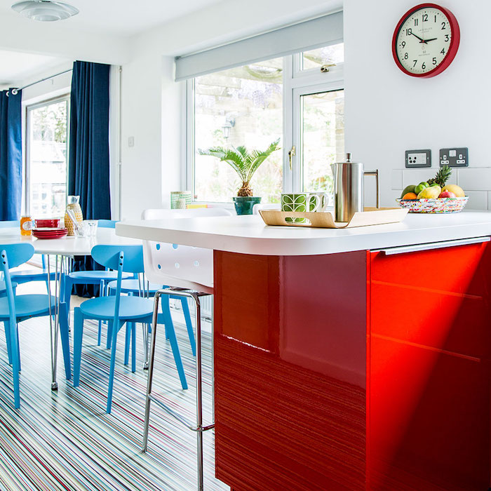 deco bleue et rouge dans une cuisine ouverte sur une salle à manger, ilot central rouge avec plan de travail blanc, table blanche et chaises bleues, fond blanc