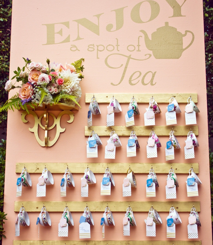 exemple de plan de table mariage, fond rose saumon, des tasses à thé suspendues avec bouquet de fleurs à côté, pause thé, petites étiquettes colorées