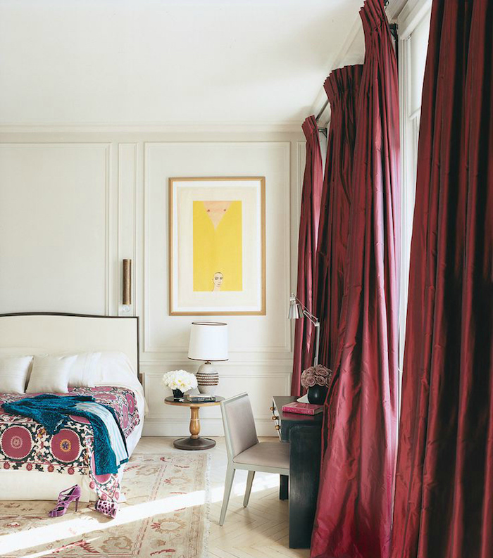 des rideaux couleur bordeau dans une chambre à coucher blanche, design, linge de lit blanc et couverture à motifs orientaux, tapis usé, parquet blanchi