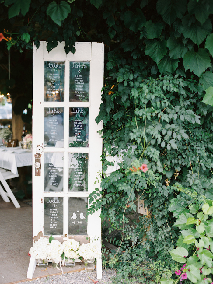 idée de plan de table mariage original, une porte vintage avec les noms des invités écrits sur les carreaux de verre, liste écrite en feutre blanc verre, cadre naturel