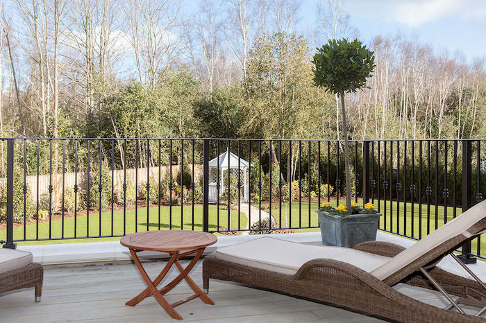 aménager sa terrasse, chaise longue en rotin gris, revêtement sol en bois clair, table basse en bois marron, arbre couronne verte, vue sur un jardin
