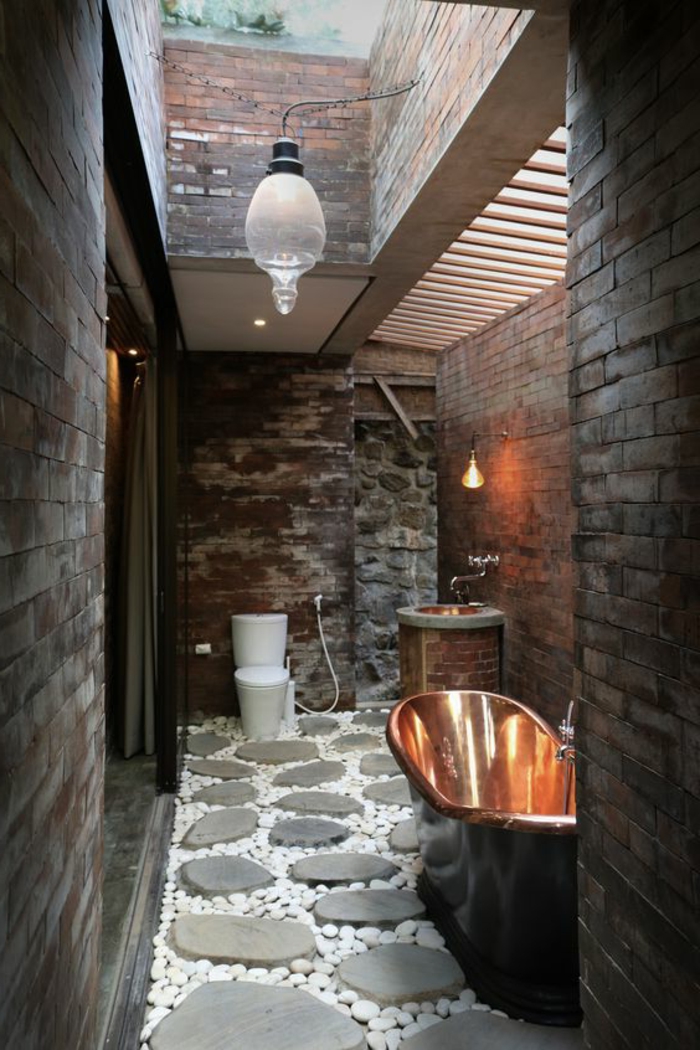idées déco salle de bain, sol en pierres et galets, baignoire cuivrée, murs en briques