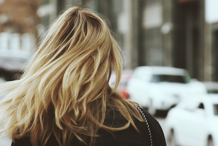 mèches-blondes-sur-cheveux-bruns-manteau-noir-coiffure-femme-cheveux-raides tie and dye cheveux mi long, promenade en ville femme, manteau en noir, cheveux racines foncées