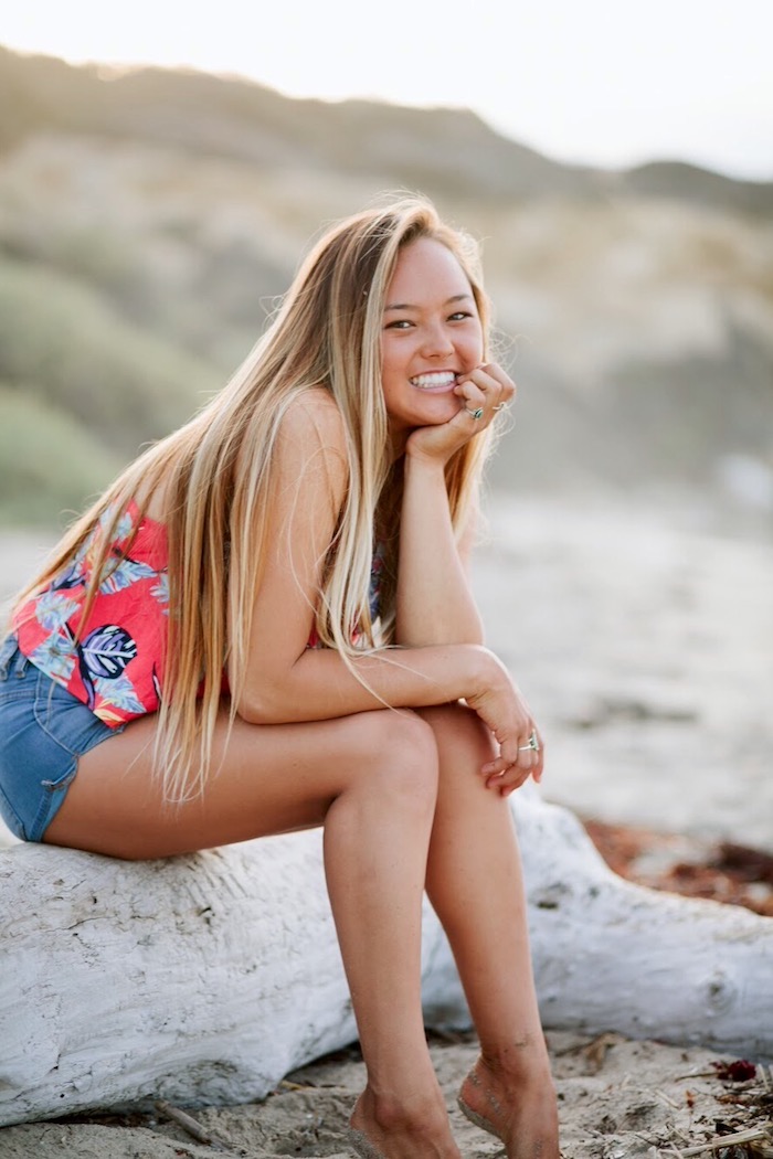 meche-blonde-shorts-en-denim-bague-en-or-avec-pierre-turquoise-débardeur-rose-foncé-a-motifs-feuilles balayage sur cheveux chatain, débardeur femme à motifs tropicales, cheveux longs à mèches blondes