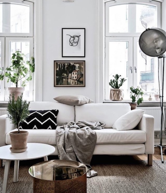 deco esprit scandinave avec canapé blanc, couverture gris et coussins décoratifs noir, blanc et gris, table basse blanche, mur blanc, deco de plantes vertes
