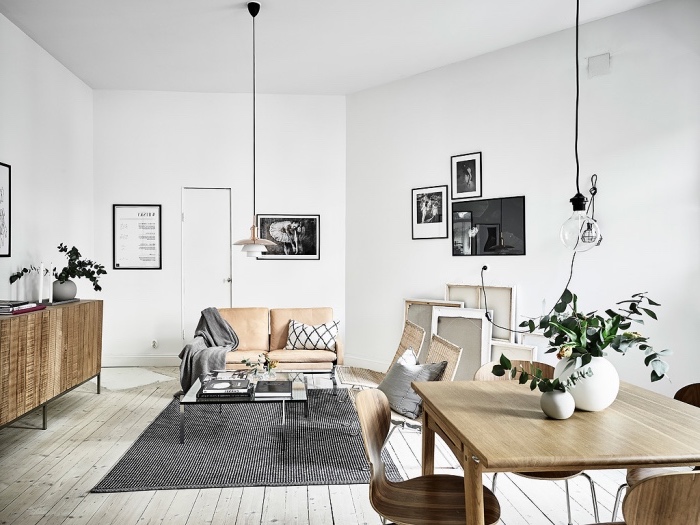 meubles scandinaves dans un salon, canapé eux places en cuir, tapis noir et blanc, table et chaises bois dans un coin salle à manger, parquet gris clair, deco murale graphique
