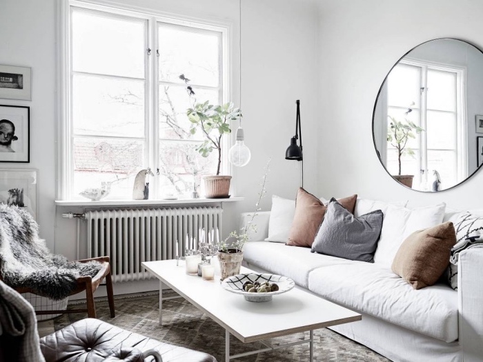 meubles scandinaves dans un salon moderne, canapé blanc, coussins gris et marron, table basse blanche, tapis gris à formes géométriques, chaise peau animal grise, intérieur blanc, miroir rond