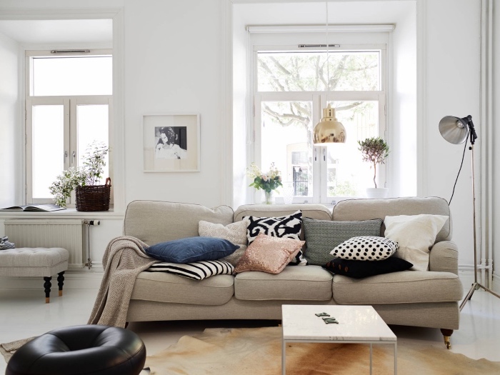 mobilier scandinave dans un salon moderne nordique avec canapé gris, tapis peau animal, peinture murale blanche, assise noire en cuir, coussins colorés, suspension dorée
