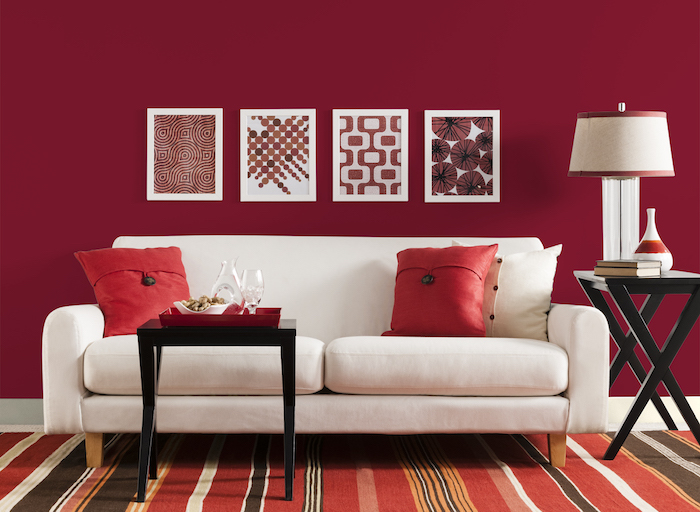 peinture murale couleur framboise dans un salon dominé par le rouge, tapis à rayures rouge, orange, marron, table basse noire, canapé blanc contrastant